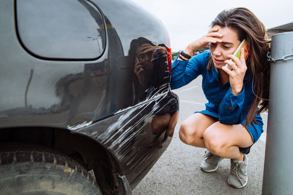 worried woman making a call over her damaged car hit and run