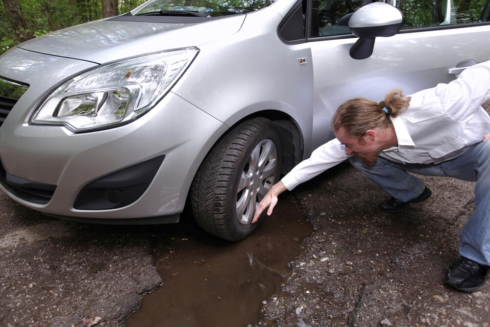 upset man looking at pothole damage to his car how to avoid potholes