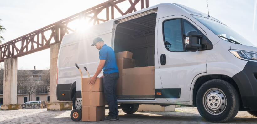 Delivery driver unloading boxes from a cargo van during a work shift, showing the daily activity protected by delivery driver car insurance.