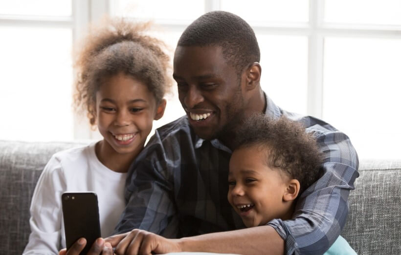 african american man with his kids staying connected with a smart phone social distancing