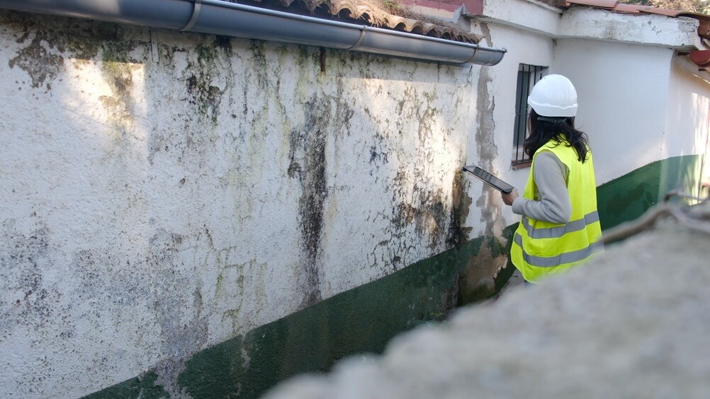 Home inspector examining exterior wall water and structural damage after a severe storm, representing tornado home insurance assessment and repairs.