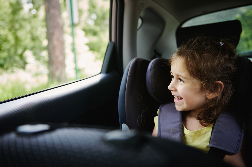 Young child sitting in a booster seat in the back seat of a car.
