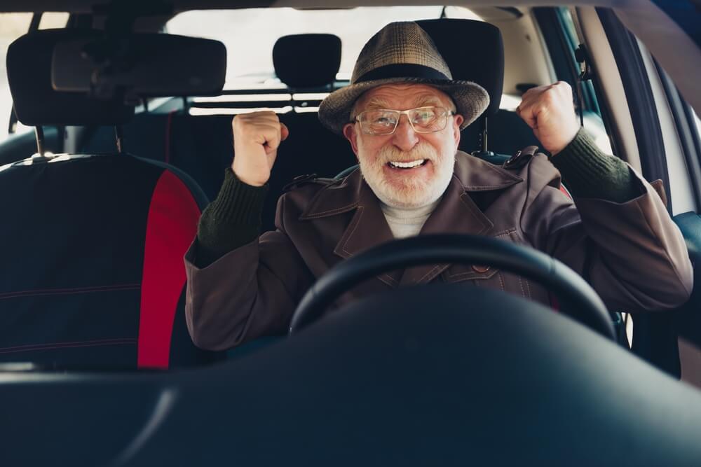 Happy senior driver celebrating inside his car, illustrating how auto insurance age brackets can affect coverage for older motorists.