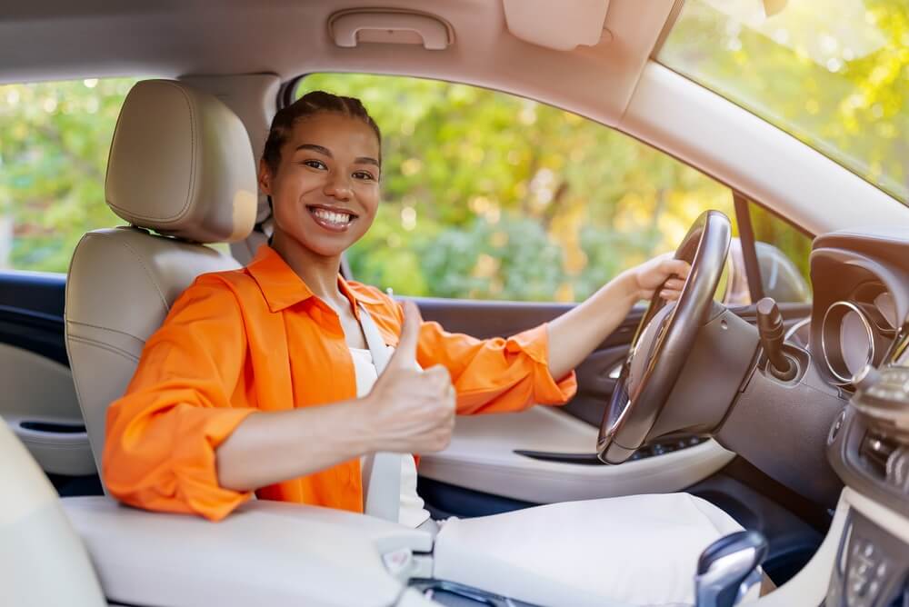 Young woman smiling behind the wheel and giving a thumbs-up, illustrating auto insurance age brackets for confident drivers.