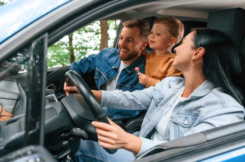 Smiling family buckled up inside a car during a road trip, illustrating auto insurance age brackets.