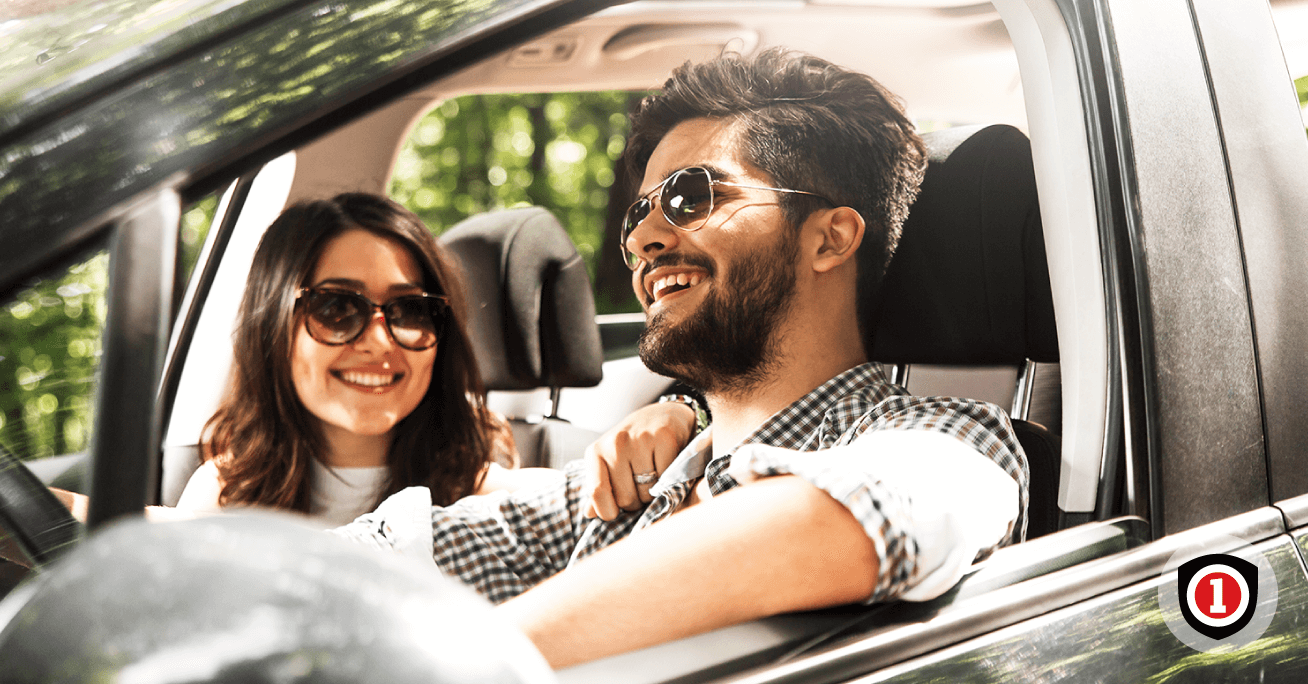 Hispanic couple Driving and smiling while they're covered by Auto Insurance