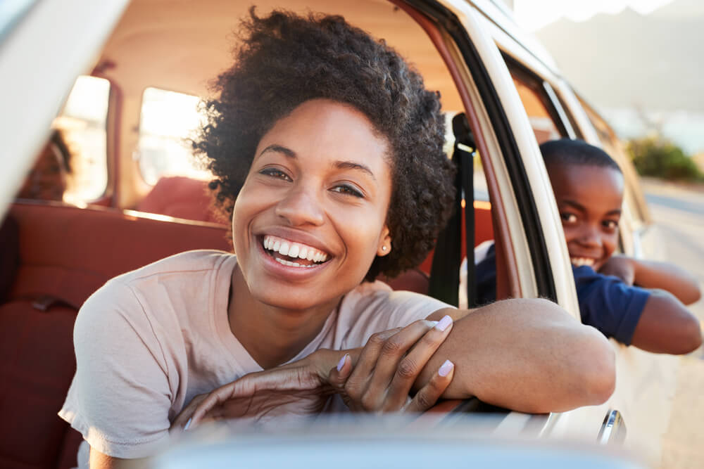 african american mom with her child on a car with umbrella coverage