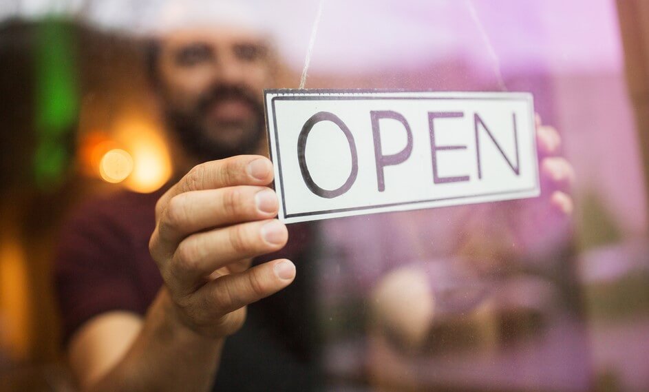 man putting an open sign on his shops door