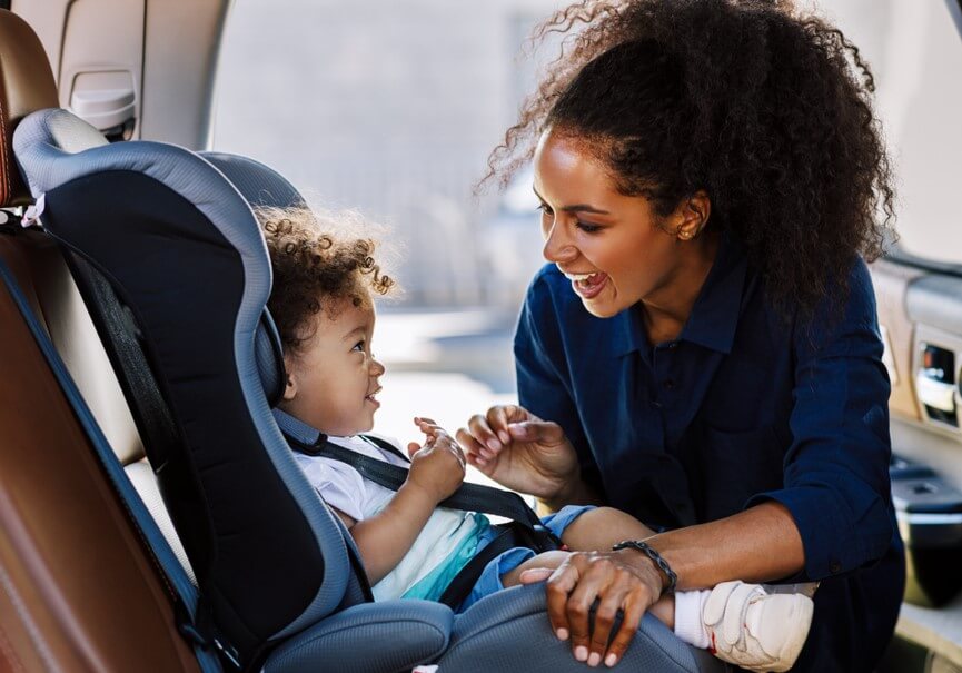 happy african american mother strapping traveling with children in car seat