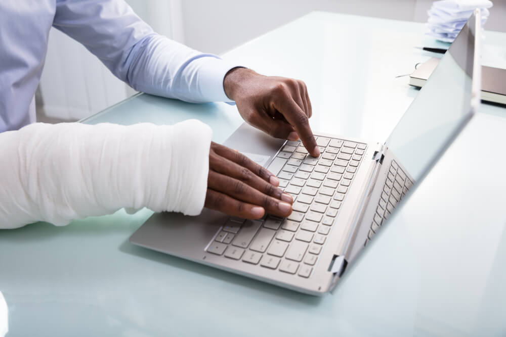 Close-up Of A Businessman With Bandage Hand Using Laptop At Workplace asking how does disability insurance work