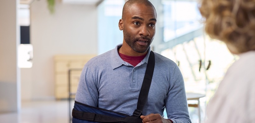 Employee with an injured arm discussing paperwork with a representative, illustrating the importance of disability insurance for employees.