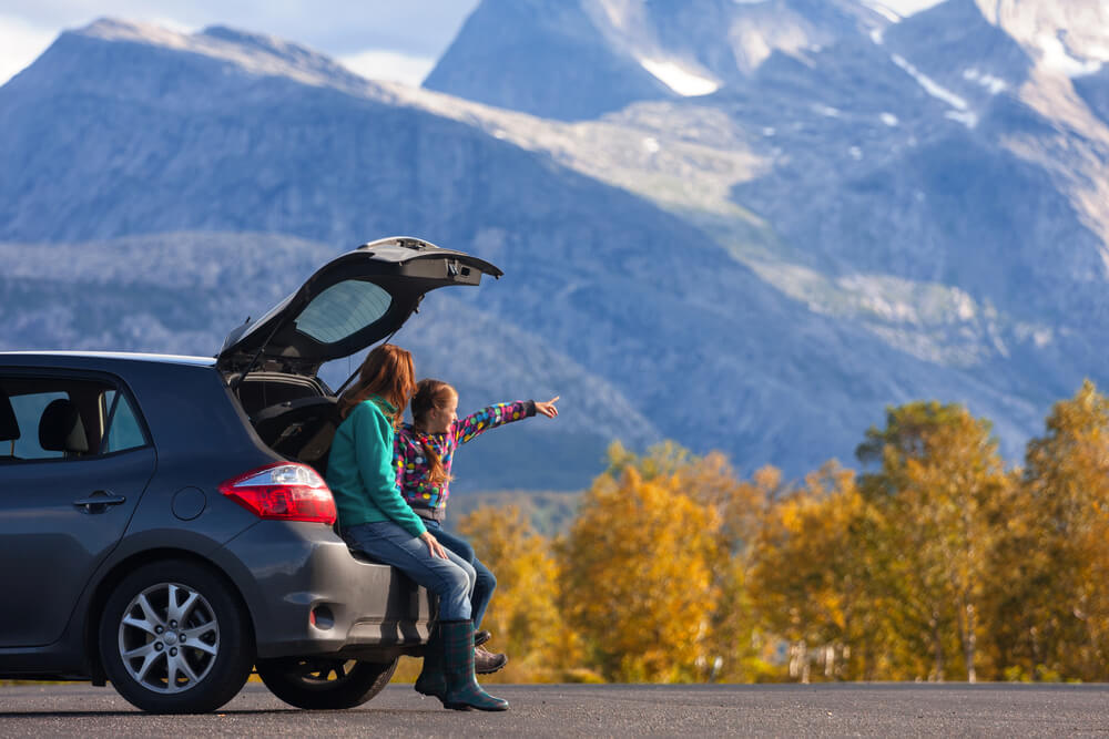 mom and daughter on the back of a car looking at scenery while on safe vacation