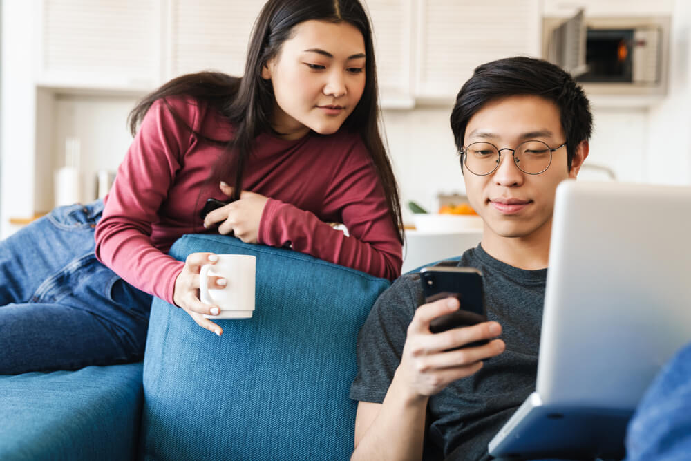 youngasian couple looking for life insurance in their phone and laptop