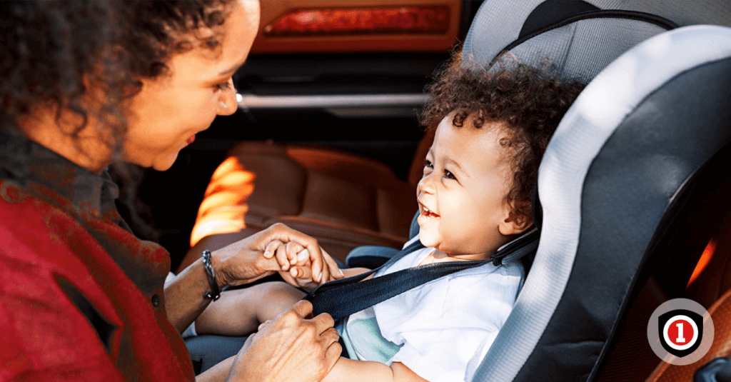 A mother playing with her child while he's sitting on his car seat 