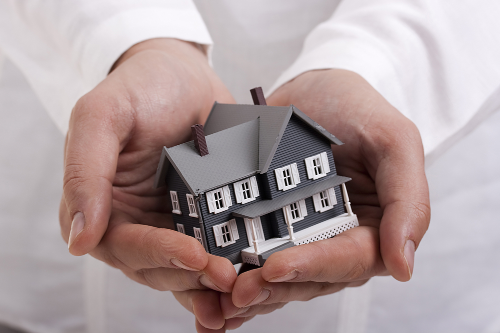 Man in white holding a model of a house in his hands.