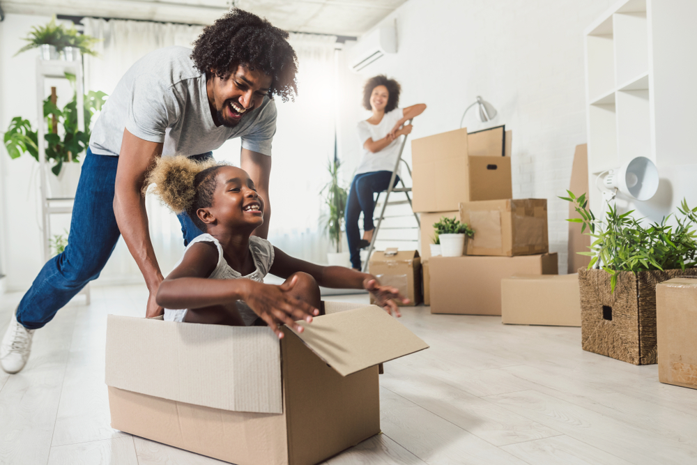 African American couple with dad sliding child across floor of new home in a box