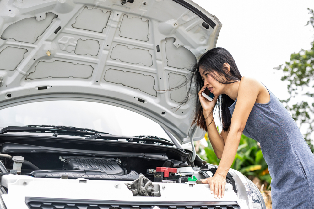 Young Asian woman on phone with hood of car up