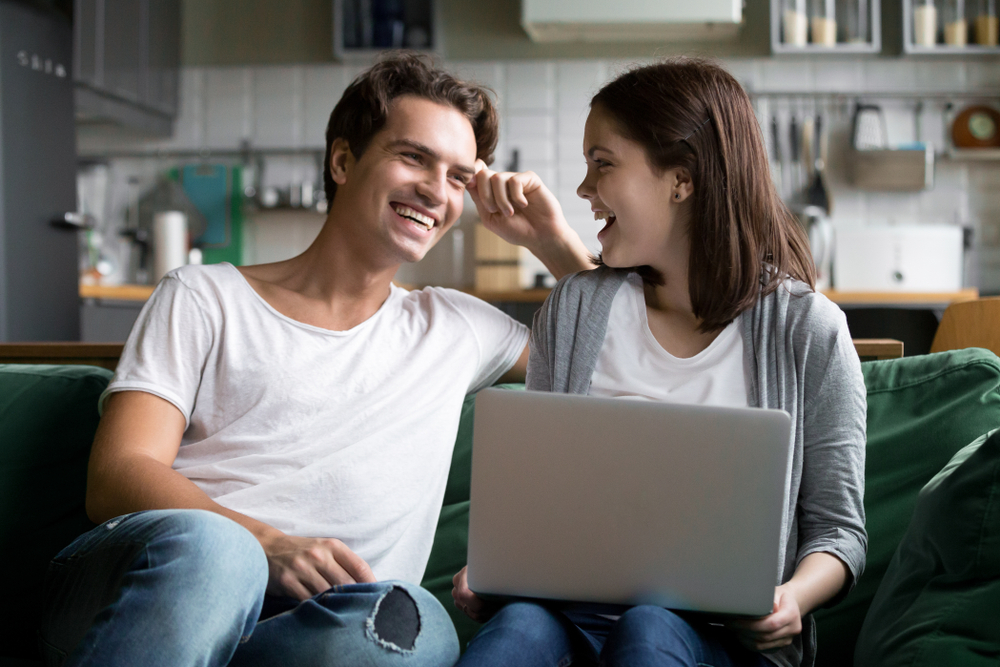young couple on couch with laptop looking at life insurance options