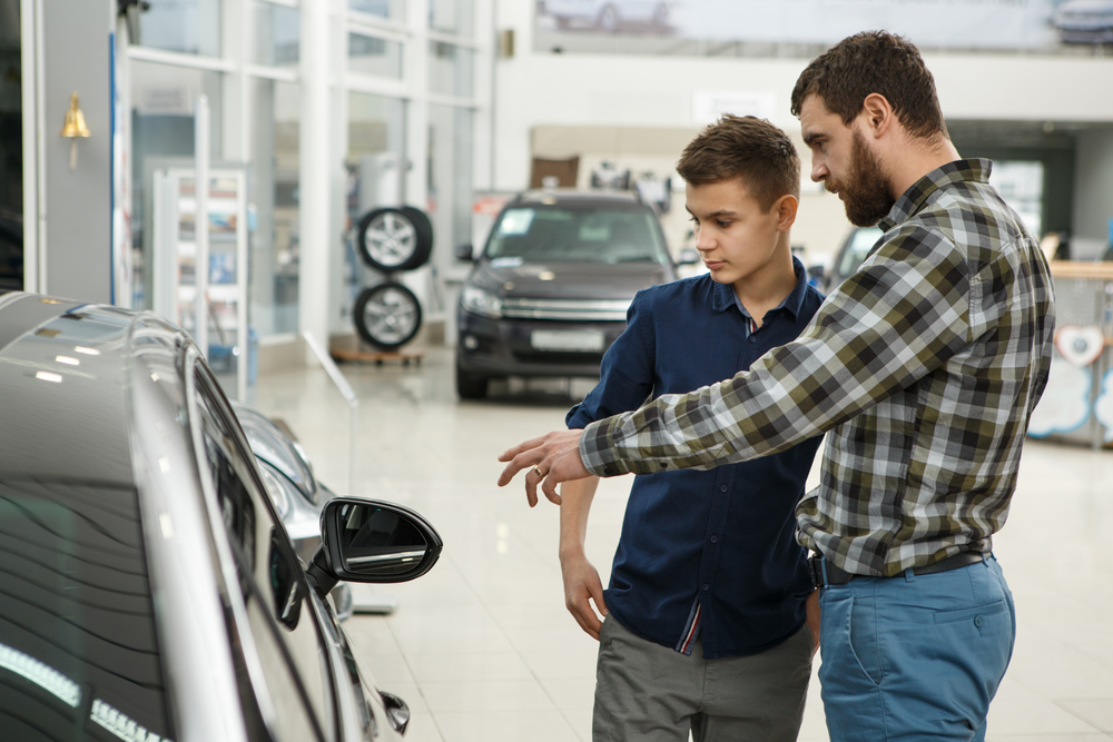 father standing next to new car with teenager
