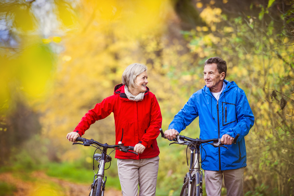 Older couple smiles as they walk their bicycles through the woods