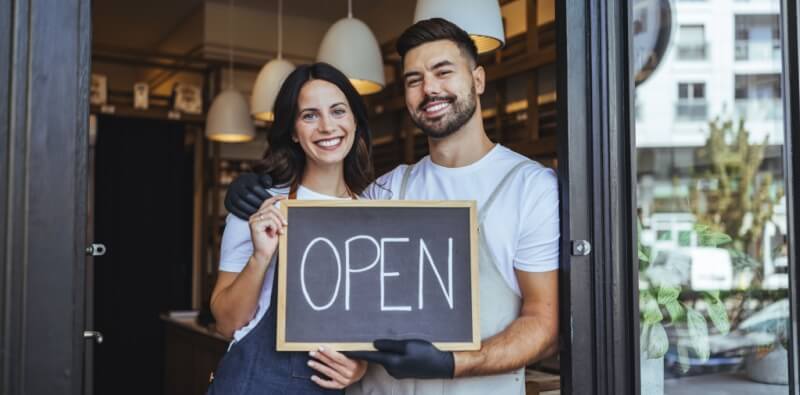 Small business owners standing outside their storefront, representing business expansion and the impact a second location can have on commercial insurance coverage.