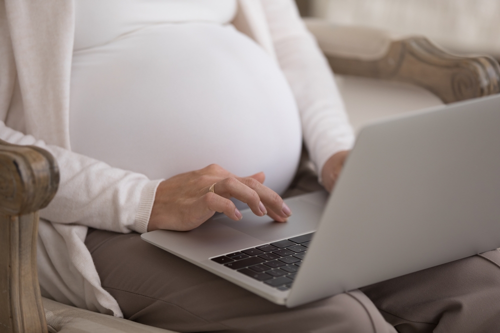 Cut-out shot of an unknown pregnant woman sitting in an armchair using a laptop to buy life insurance.