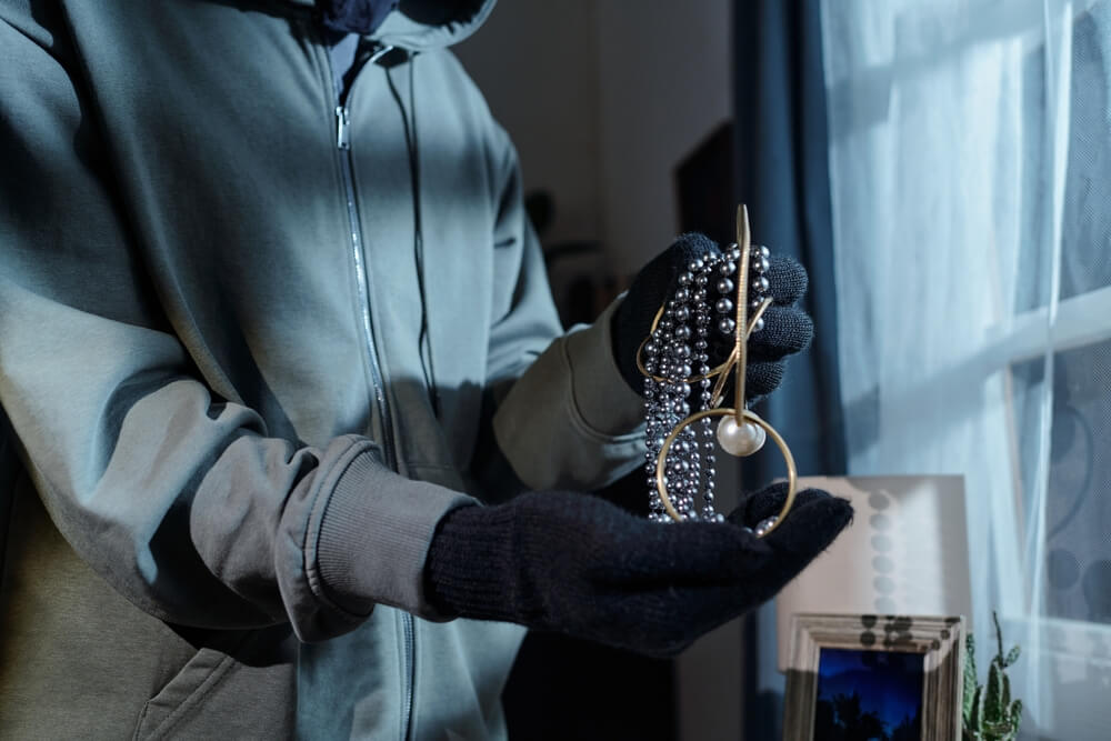 Thief holding stolen jewelry inside a home, showing why valuable items home insurance may not fully cover may require extra protection.