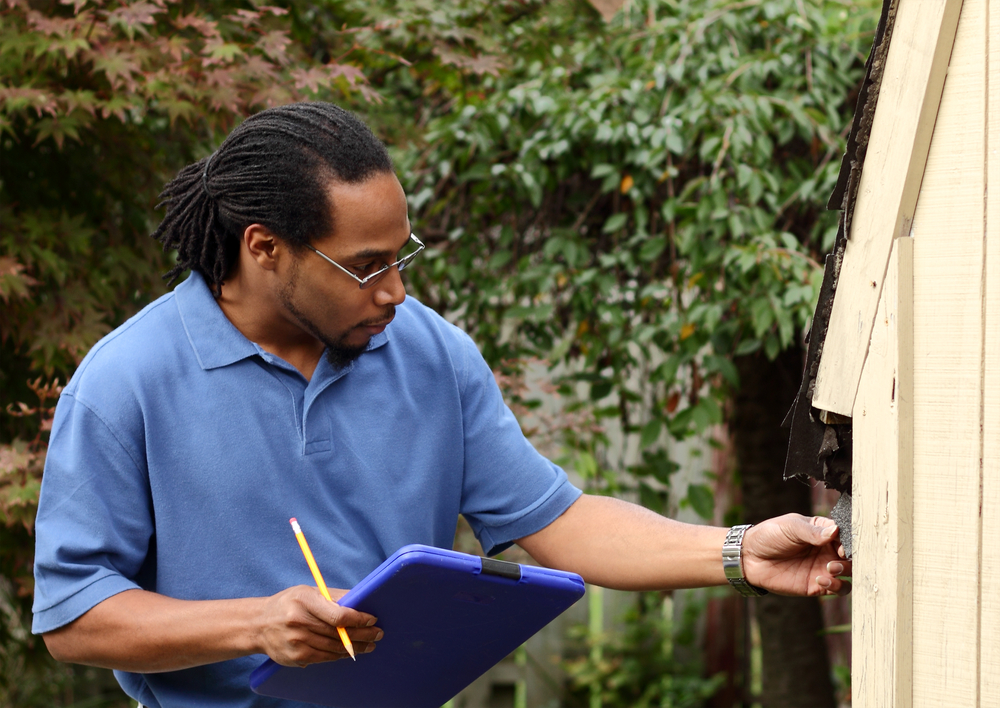 African American insurance inspector looks at faulty roof shingles