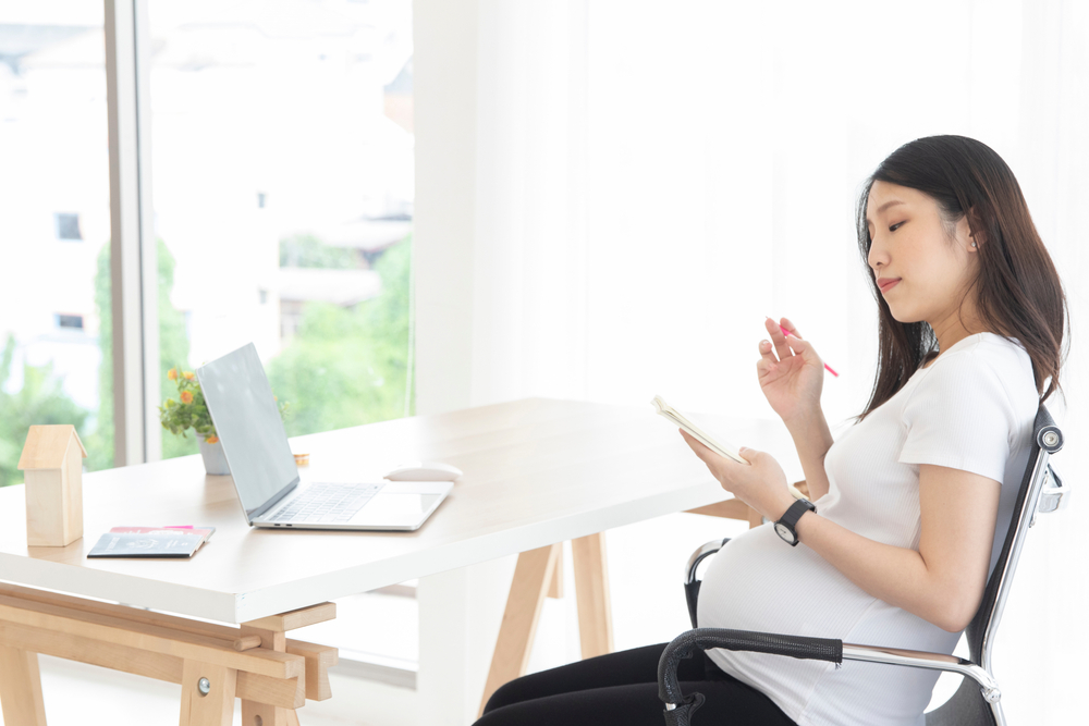 Pregnant Asian woman examines her workplace benefits