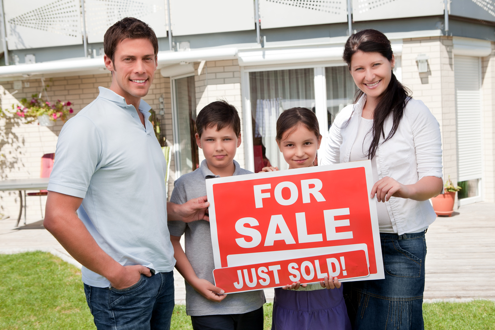 Family holds for sale sign with just sold sign in front of house