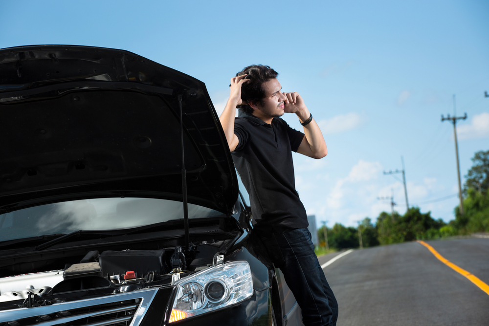 Asian man is on his phone with hood of car open