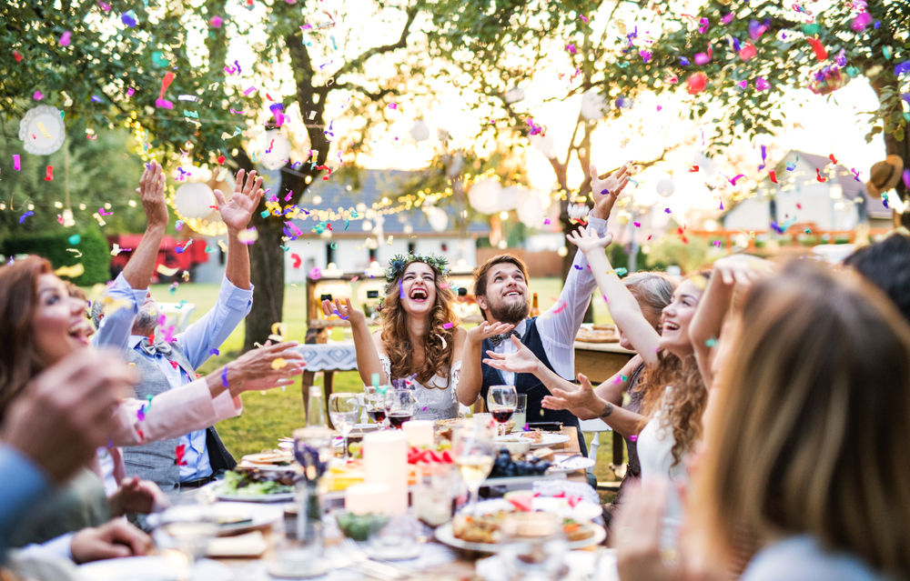 Bride,And,Groom,With,Guests,At,Wedding,Reception,Outside,In Couple celebrating outdoor wedding reception