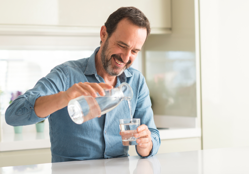 Smiling man pours himself a glass of water - life insurance at InsureOne