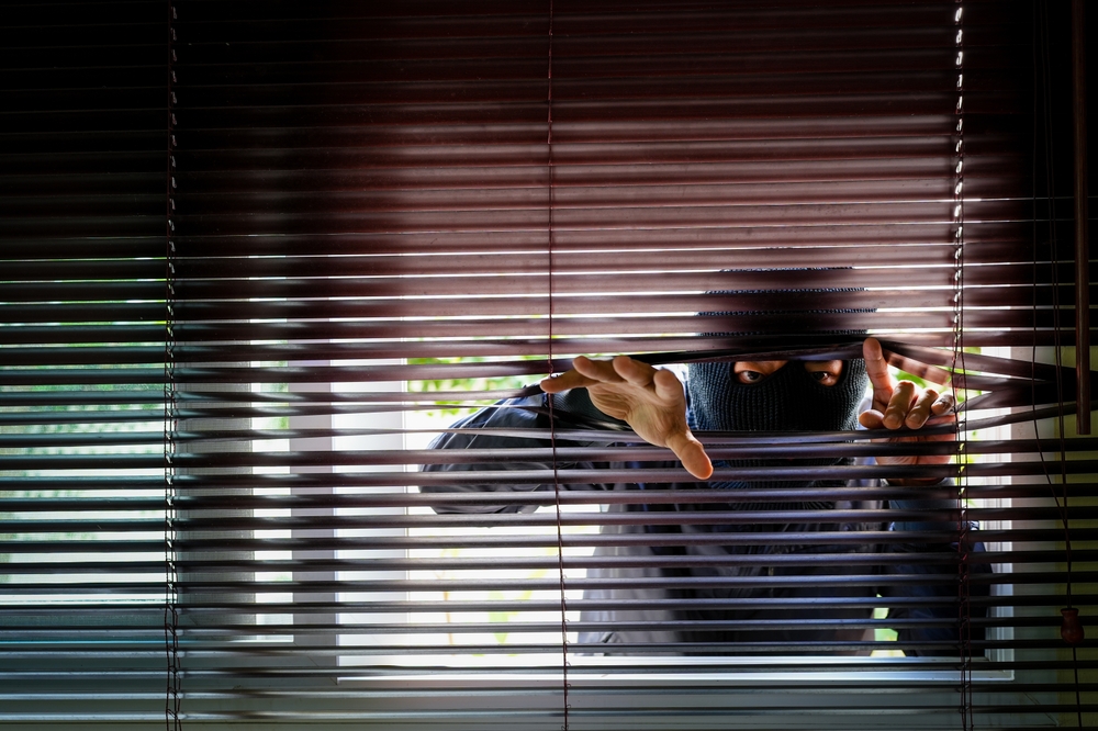 Burglar in a ski mask peering through the blinds of the window - best home insurance
