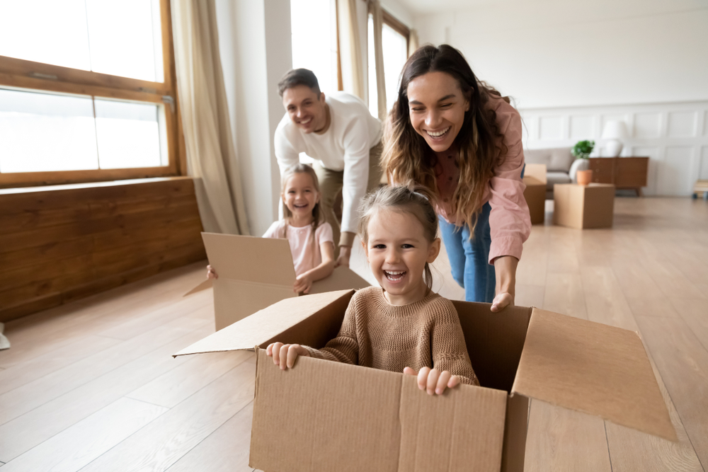 Happy young family with mom and dad pushing daughters across the floors of their new home in boxes - best homeowners insurance.