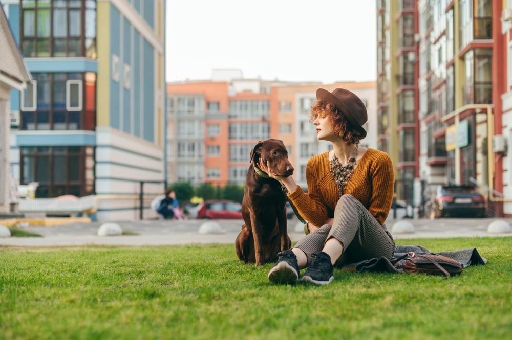 Young woman in a hat sits with her chocolate lab on her apartment complex lawn - best renters insurance.