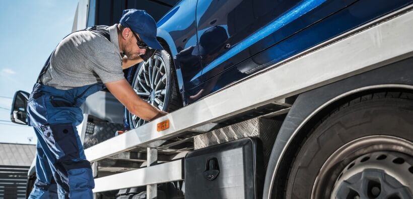 Tow truck operator carefully securing a vehicle on a flatbed truck, a common roadside scenario where drivers often wonder when to tip roadside assistance.