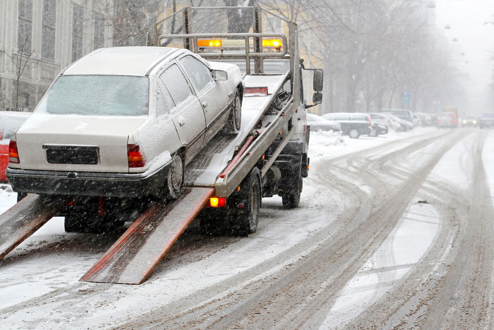 Tow truck driver hauling off car in the snow.