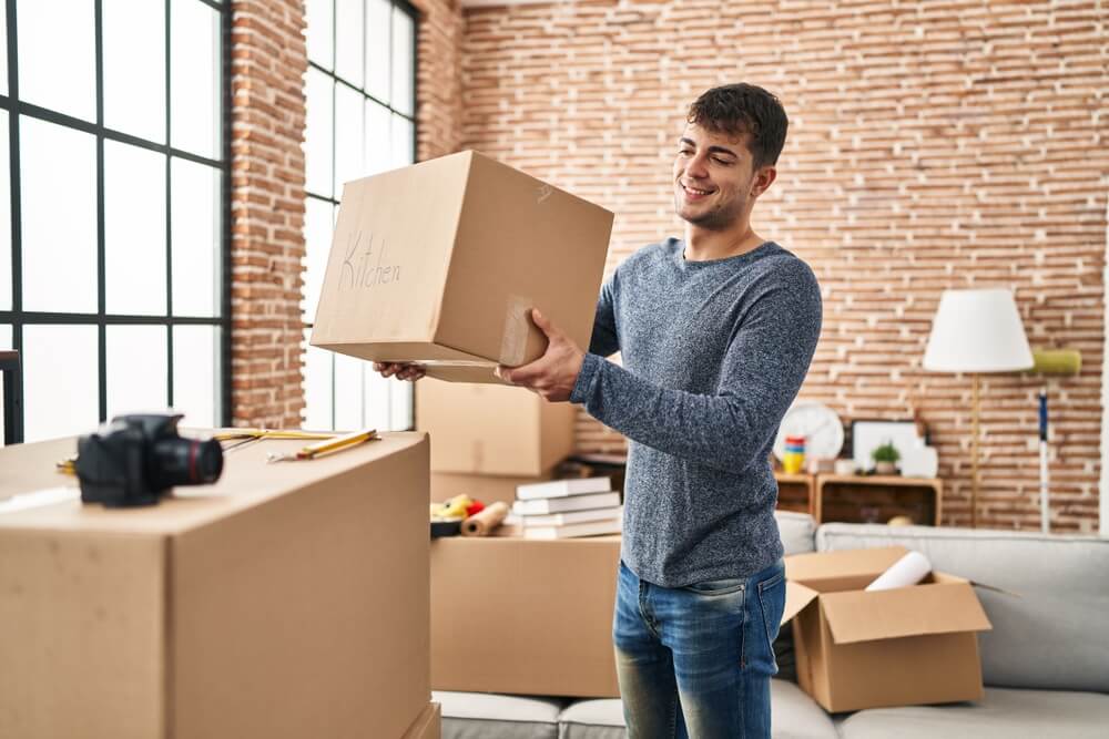 insure-one-is-renters-insurance-required-for-tenants-1 Young man unpacking boxes in his new apartment - best renters insurance.