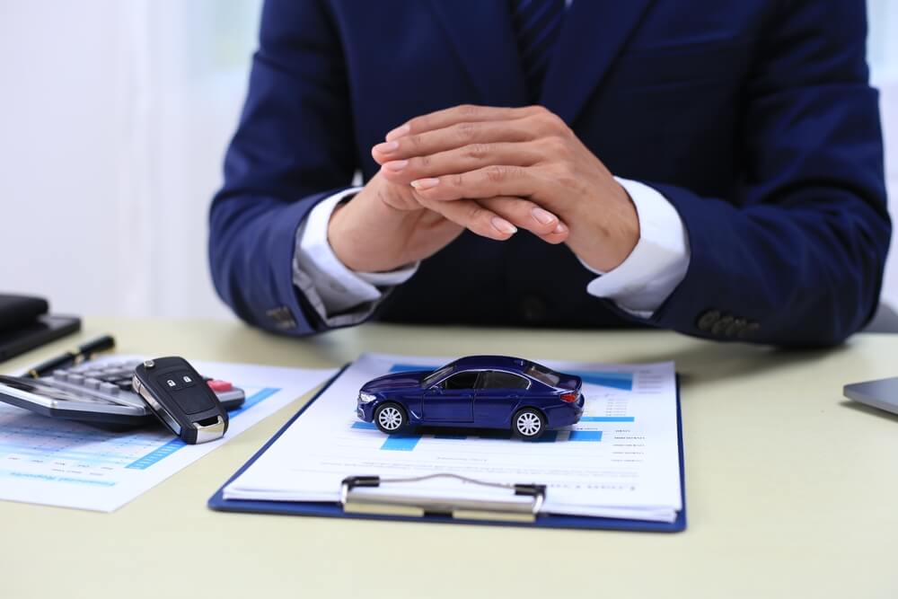 Insurance agent reviewing documents with a model car and rental car keys on a desk, representing rental car coverage and policy discussion.