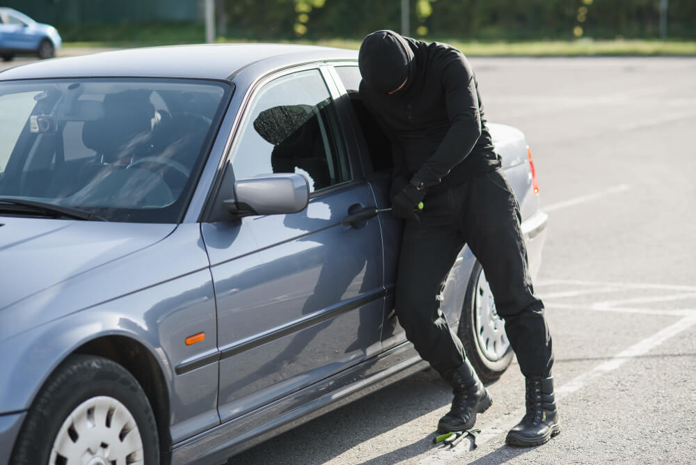 A person dressed all in black breaks into a car with plans to steal it - best car insurance.