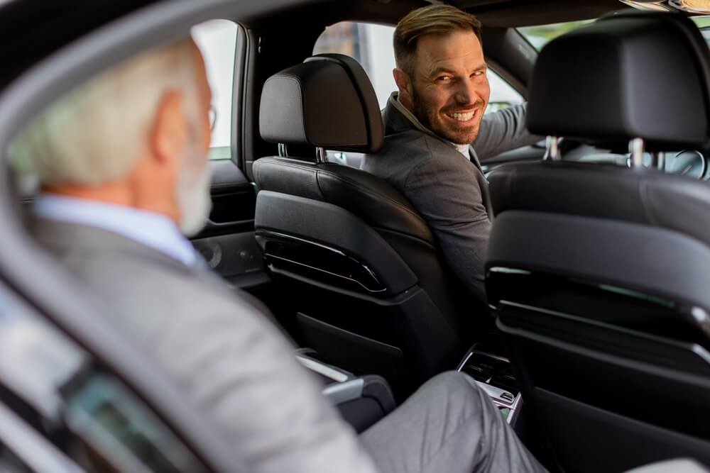 A rideshare driver turns around to smile at his passenger, an older man - best car insurance/
