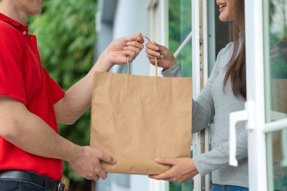 ion-the-effects-of-ridesharing-and-delivery-jobs-on-personal-auto-insurance-2 A delivery driver hands a bag of food to a woman in her house - best car insurance.