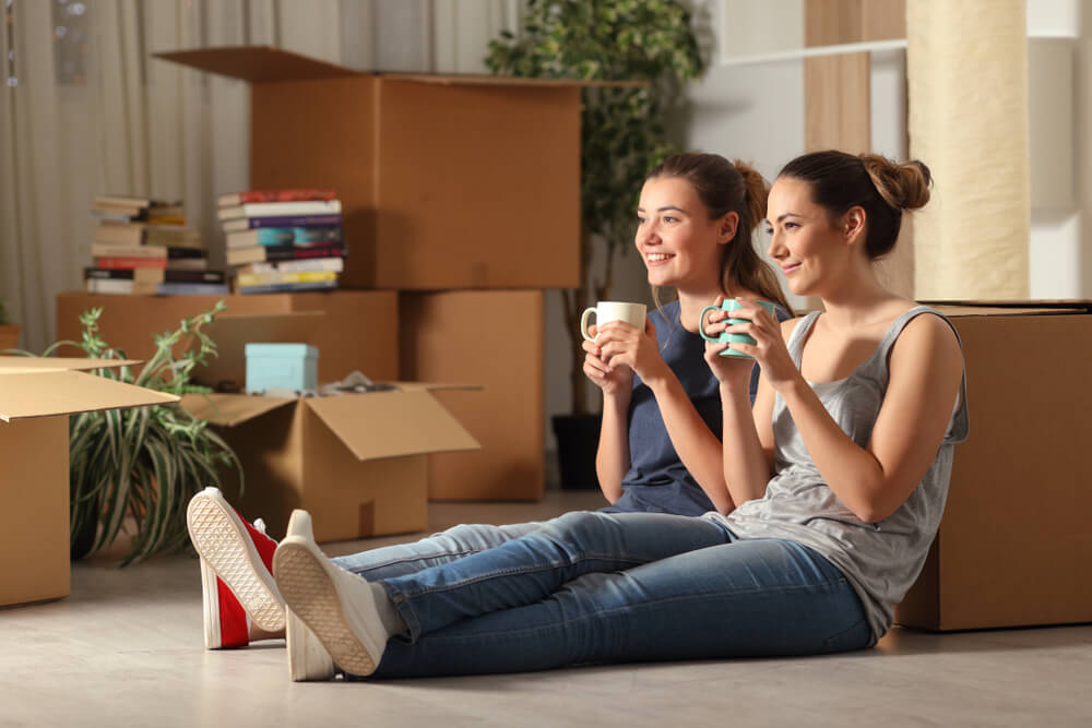 Two roommates drink warm tea in their new apartment, smiling because they have the best renters insurance.