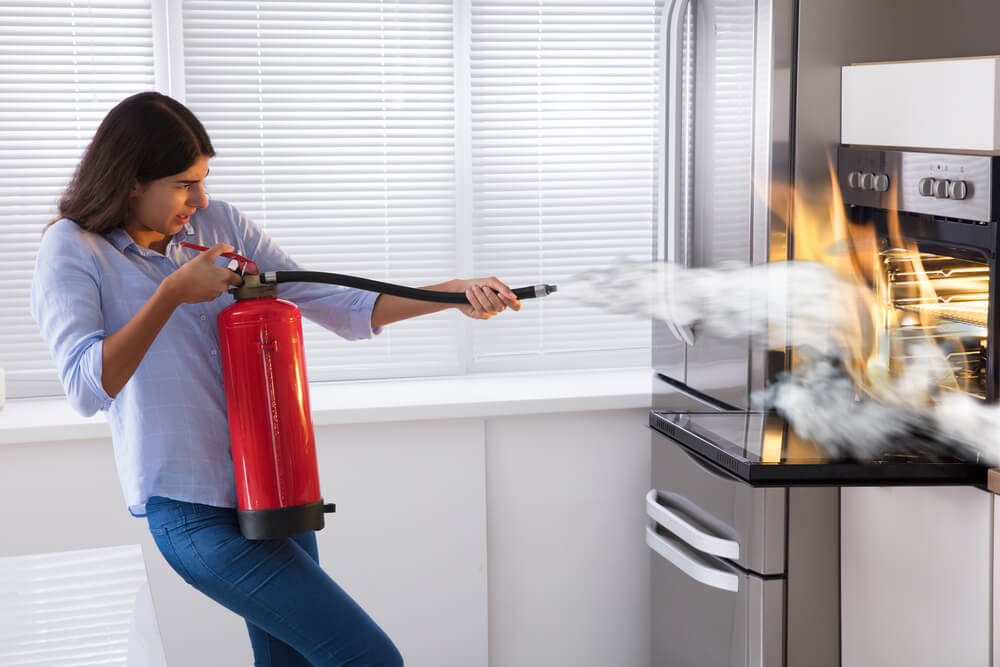 ion-does-home-insurance-cover-fires-1 Young woman using fire extinguisher to put out fire from oven at home, home insurance and fires.