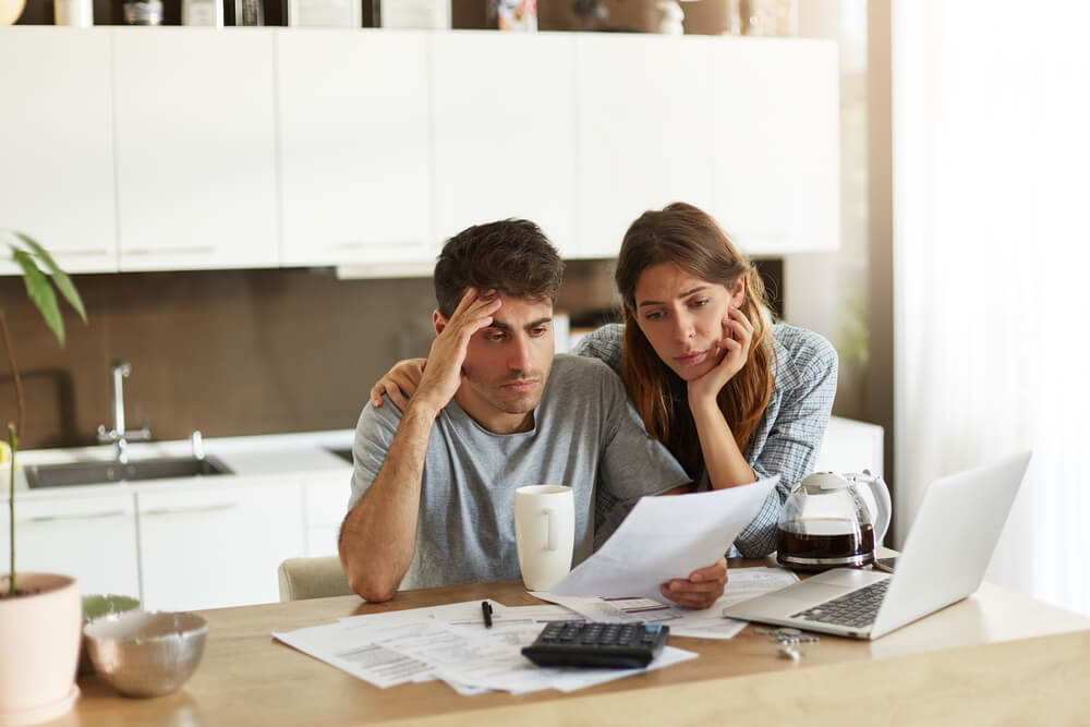 ino-are-you-overpaying-for-insurance-1 Unhappy American couple managing home accounts in kitchen, trying to save some money by cutting family expenses, figuring out if they are overpaying for insurance, finding best insurance options.