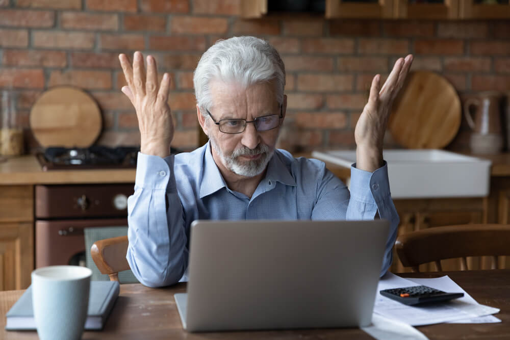 Annoyed worried aged man sit by laptop unable to make sense of overcharging on his insurance bill, overcharging and how to find the best insurance.