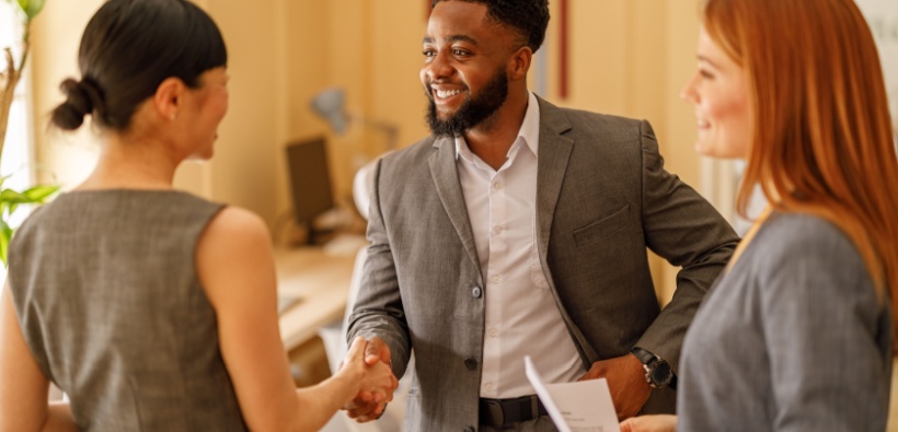 Male entrepreneur smiling and shaking hands with female partners in a modern workspace, representing a business protected by insurance-1 Male entrepreneur smiling and shaking hands with female partners in a modern workspace, representing a business protected by insurance-1