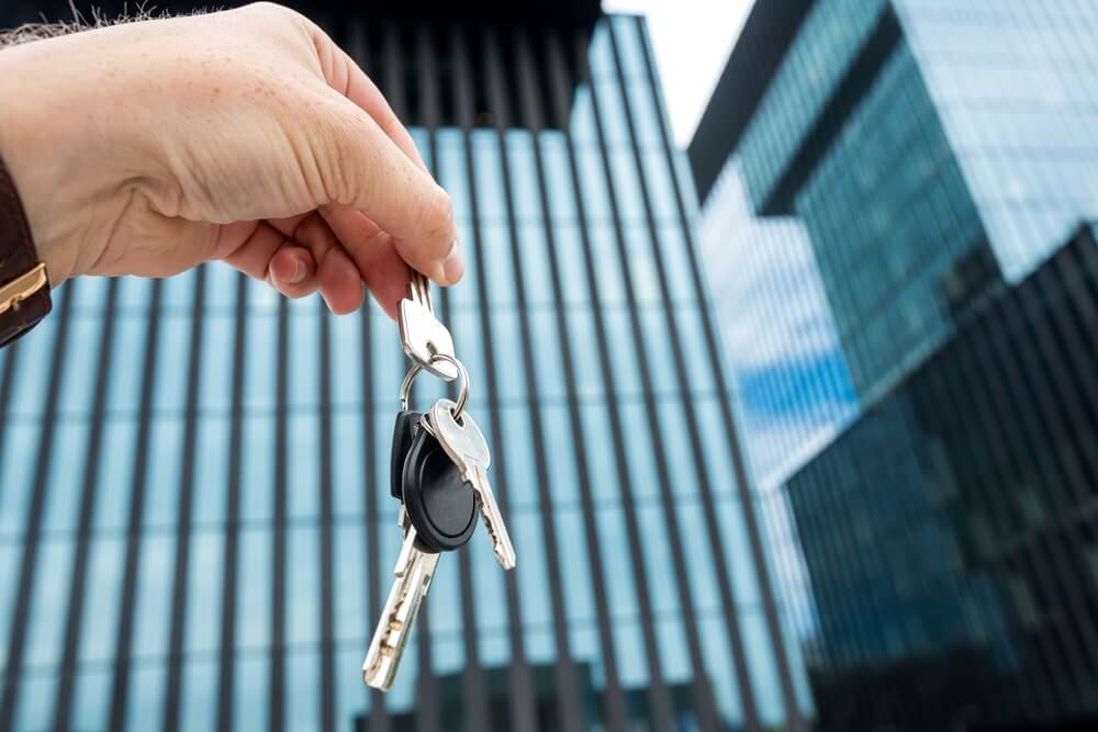 Real estate agent holding out house keys outside an office center, highlighting a business protected by insurance