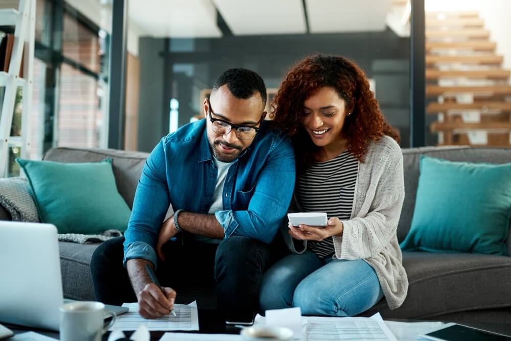 African American couple smiling while reviewing their budget at the kitchen table, happy to save with multi-policy discounts.